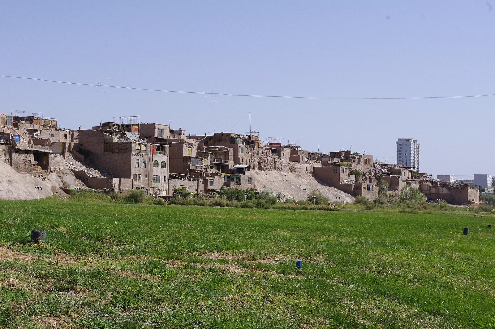 Kashgar Old City: distant view of mud-brick buildings on a hillside beyond a green field